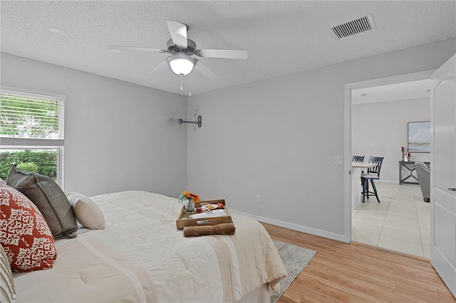 bedroom featuring visible vents, light wood-style flooring, a textured ceiling, baseboards, and ceiling fan