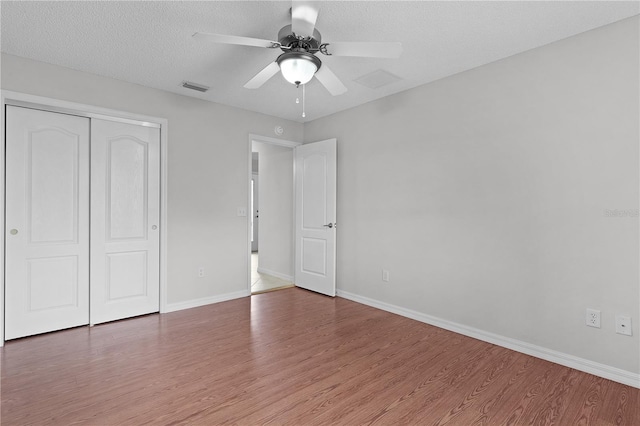 unfurnished bedroom featuring visible vents, baseboards, a closet, and wood finished floors