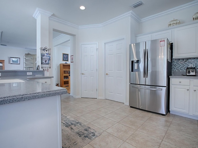 kitchen with stainless steel fridge, white cabinets, tasteful backsplash, light tile patterned floors, and ornamental molding