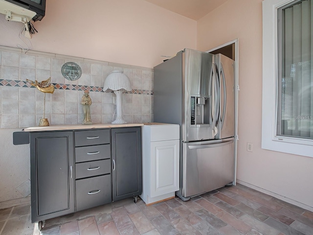 kitchen featuring gray cabinets, stainless steel refrigerator with ice dispenser, and tile walls