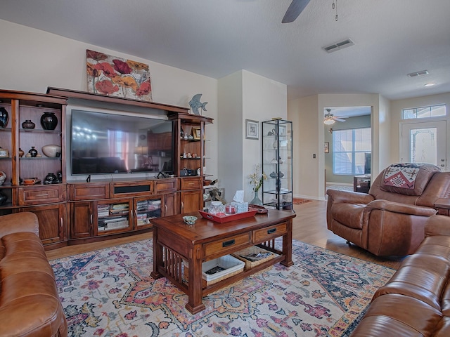 living room featuring a textured ceiling, light wood-type flooring, and ceiling fan