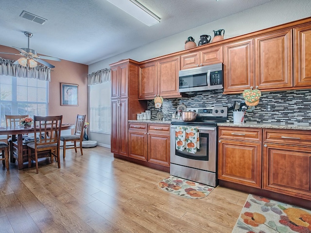 kitchen featuring stainless steel appliances, ceiling fan, light wood-type flooring, light stone counters, and tasteful backsplash