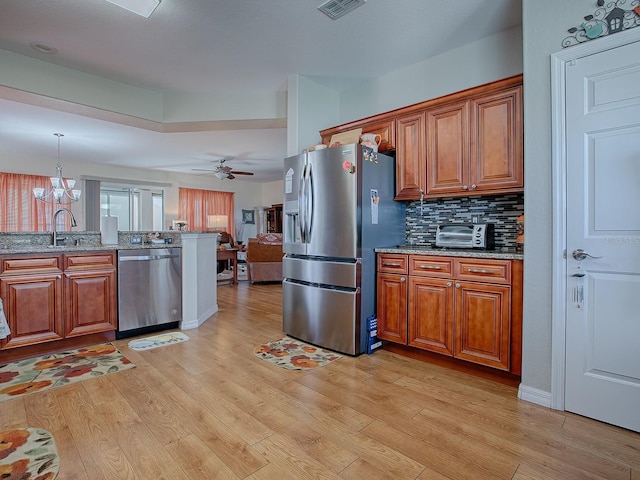 kitchen with appliances with stainless steel finishes, ceiling fan with notable chandelier, light hardwood / wood-style floors, decorative light fixtures, and light stone counters