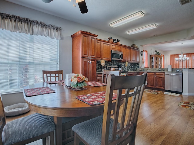 dining room with light hardwood / wood-style flooring, a textured ceiling, and ceiling fan with notable chandelier