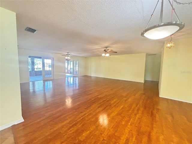 empty room with hardwood / wood-style flooring, a textured ceiling, and ceiling fan with notable chandelier