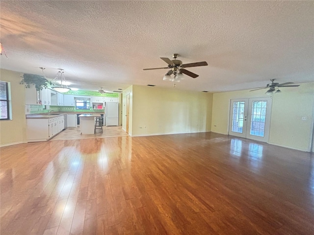 unfurnished living room with light hardwood / wood-style floors, french doors, a textured ceiling, and ceiling fan