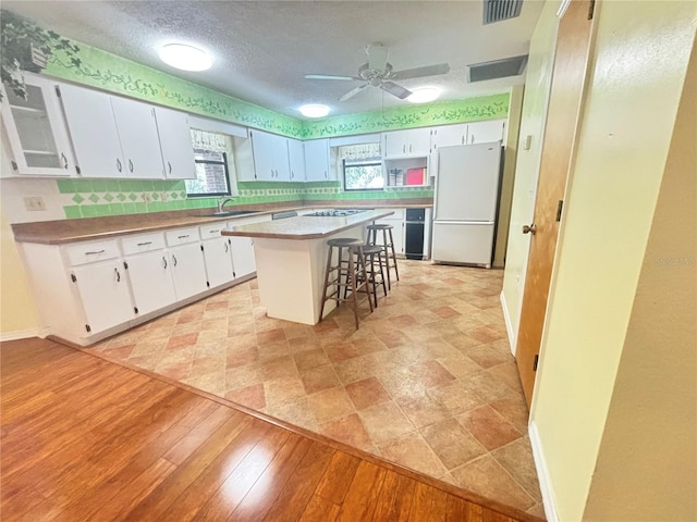 kitchen with a kitchen island, white cabinets, a kitchen bar, and white refrigerator