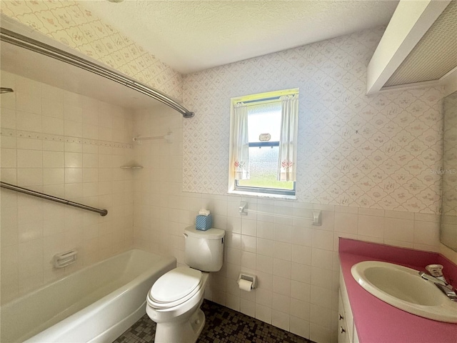 full bathroom with toilet, vanity, tiled shower / bath combo, tile walls, and a textured ceiling