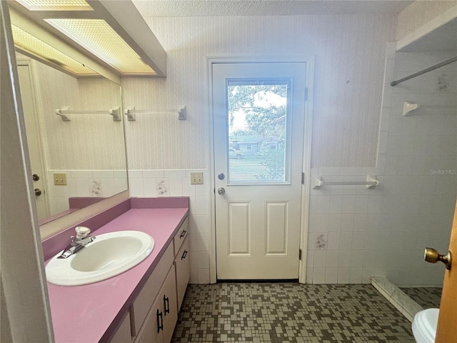 bathroom with a textured ceiling, walk in shower, tile walls, toilet, and vanity