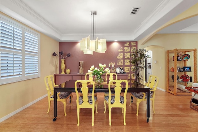 dining space with light hardwood / wood-style floors, a notable chandelier, a raised ceiling, and crown molding