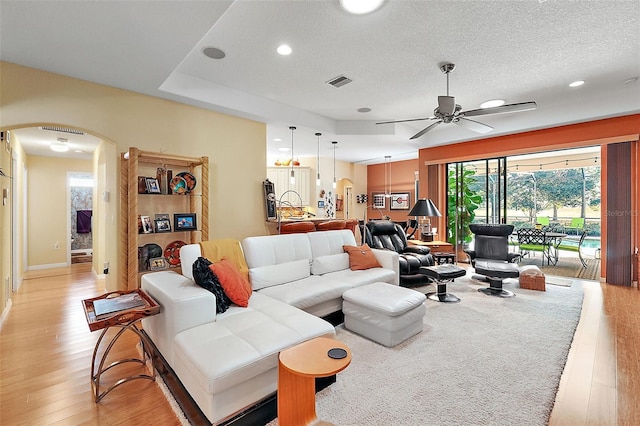 living room with light hardwood / wood-style flooring, a textured ceiling, and ceiling fan