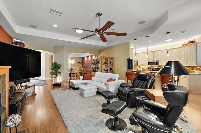 living room with ceiling fan, a textured ceiling, light hardwood / wood-style floors, and a raised ceiling