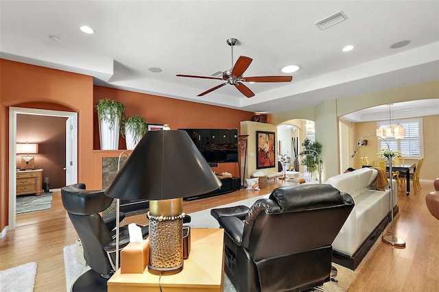 living room featuring ceiling fan with notable chandelier and light wood-type flooring