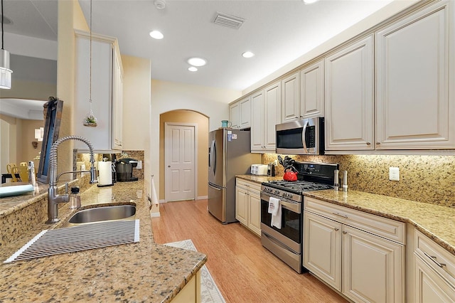 kitchen with sink, light stone countertops, decorative light fixtures, light wood-type flooring, and appliances with stainless steel finishes