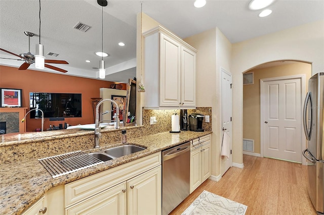 kitchen with light wood-type flooring, stainless steel appliances, cream cabinetry, decorative light fixtures, and light stone counters