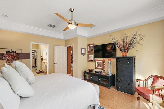 bedroom with ceiling fan, a tray ceiling, light hardwood / wood-style floors, crown molding, and ensuite bath