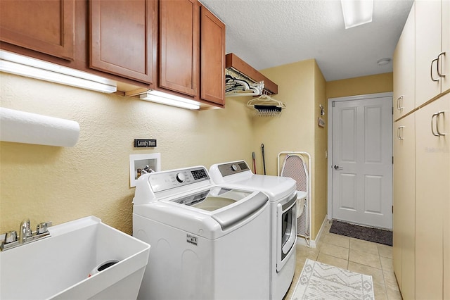 laundry room with sink, a textured ceiling, washing machine and clothes dryer, cabinets, and light tile patterned floors