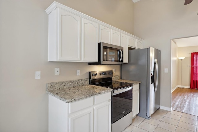 kitchen with light tile patterned flooring, light stone counters, white cabinetry, and appliances with stainless steel finishes