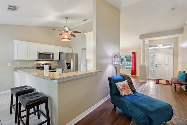 kitchen featuring lofted ceiling, kitchen peninsula, light stone countertops, white cabinetry, and stainless steel appliances