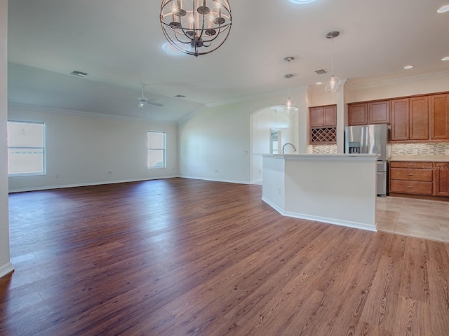 unfurnished living room featuring hardwood / wood-style flooring, ornamental molding, vaulted ceiling, and ceiling fan with notable chandelier