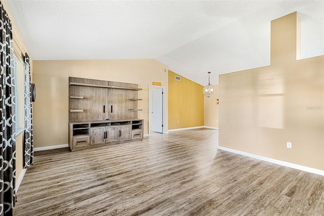 unfurnished living room featuring lofted ceiling, a textured ceiling, a notable chandelier, and wood-type flooring