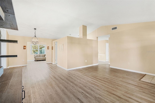 unfurnished living room featuring vaulted ceiling, hardwood / wood-style flooring, and an inviting chandelier