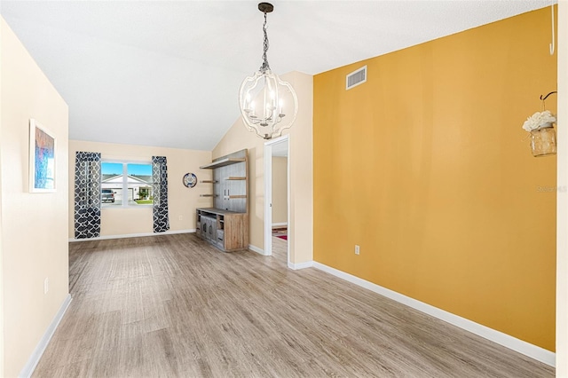 unfurnished living room with a notable chandelier, lofted ceiling, and hardwood / wood-style floors