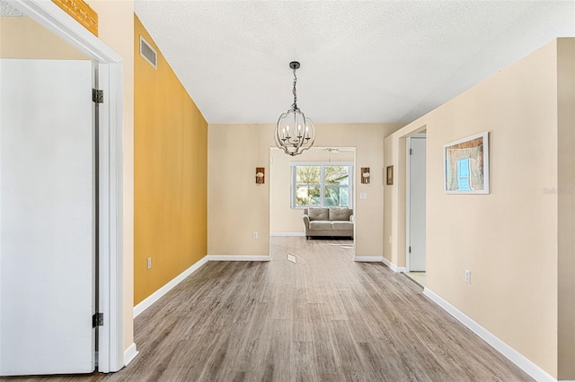 unfurnished dining area with a notable chandelier, a textured ceiling, and light hardwood / wood-style floors