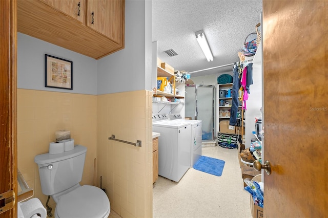 bathroom with a shower with door, washing machine and dryer, a textured ceiling, toilet, and vanity