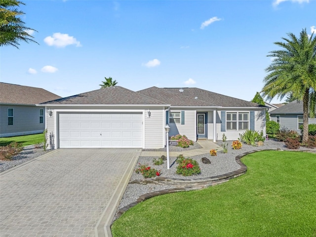 ranch-style home featuring decorative driveway, a garage, a shingled roof, and a front lawn