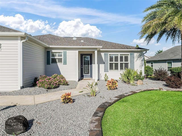 ranch-style house featuring a shingled roof and a front lawn
