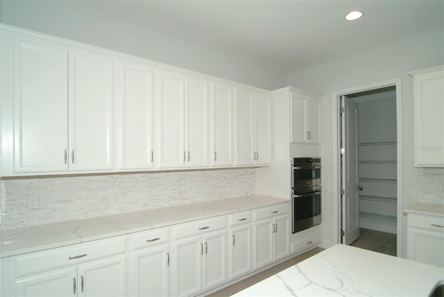 kitchen featuring white cabinets, light stone countertops, and stainless steel double oven