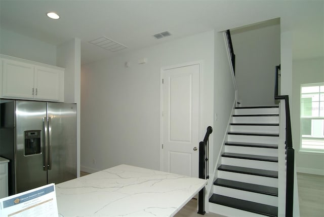 kitchen with a kitchen island, stainless steel fridge with ice dispenser, white cabinetry, light stone countertops, and light hardwood / wood-style floors