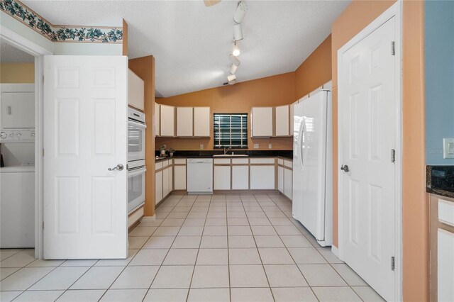 kitchen with white appliances, light tile patterned floors, a textured ceiling, and stacked washer and dryer