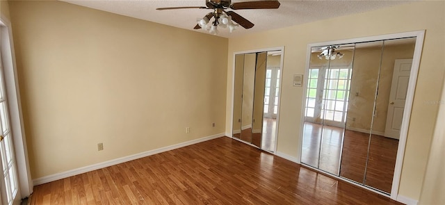 unfurnished bedroom featuring ceiling fan, a textured ceiling, wood-type flooring, and multiple closets