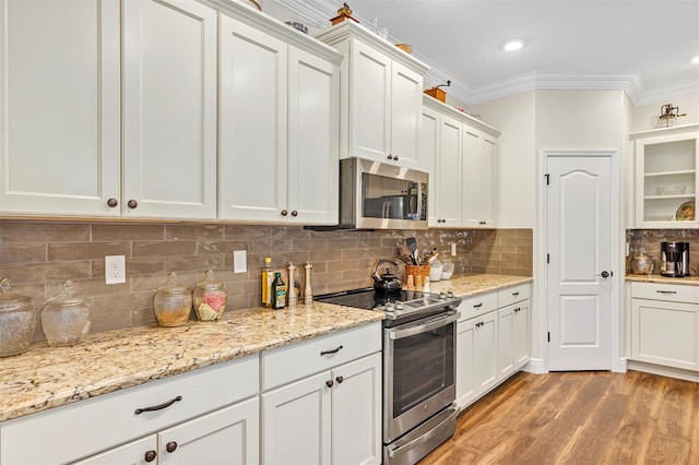 kitchen featuring white cabinets, ornamental molding, backsplash, light wood-type flooring, and appliances with stainless steel finishes