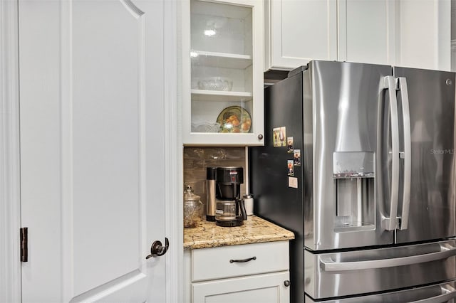 kitchen with backsplash, stainless steel refrigerator with ice dispenser, light stone counters, and white cabinets