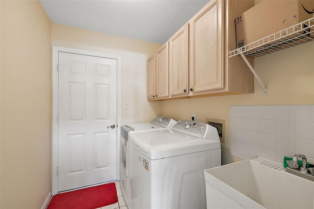 clothes washing area with sink, light tile patterned floors, a textured ceiling, washing machine and dryer, and cabinets