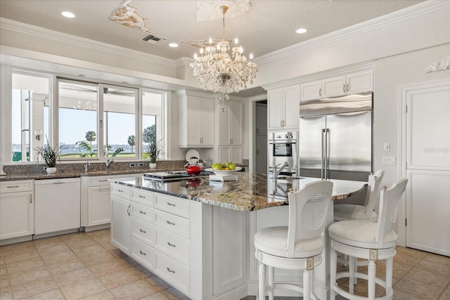 kitchen with appliances with stainless steel finishes, white cabinetry, a center island, and dark stone counters