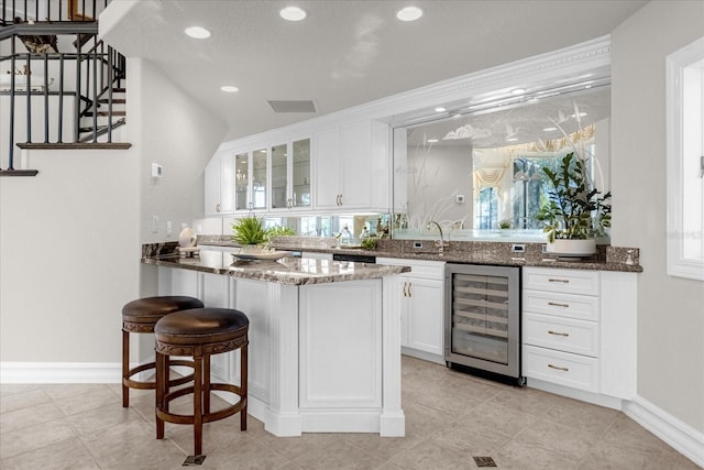 kitchen with a wealth of natural light, white cabinets, dark stone counters, and beverage cooler