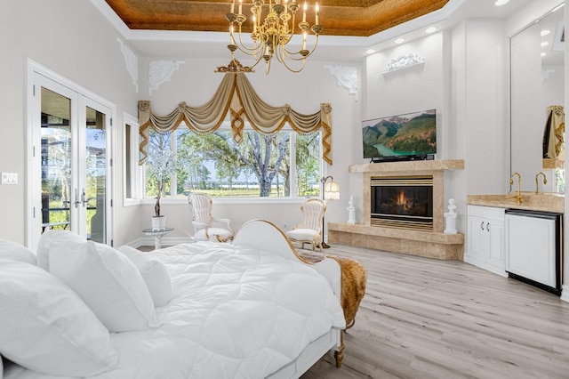 bedroom with multiple windows, access to outside, a tray ceiling, and light wood-type flooring