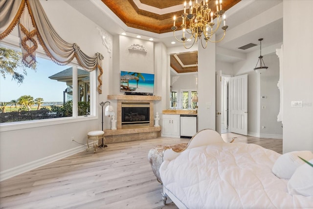 bedroom with an inviting chandelier, light hardwood / wood-style flooring, a tray ceiling, and a fireplace