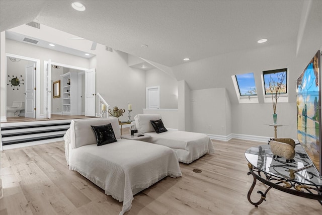 bedroom featuring vaulted ceiling with skylight, light hardwood / wood-style flooring, and a textured ceiling