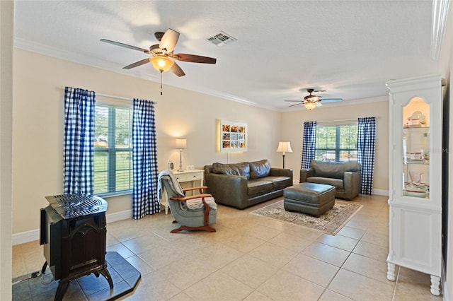 living room featuring ceiling fan, light tile patterned floors, visible vents, a wood stove, and crown molding