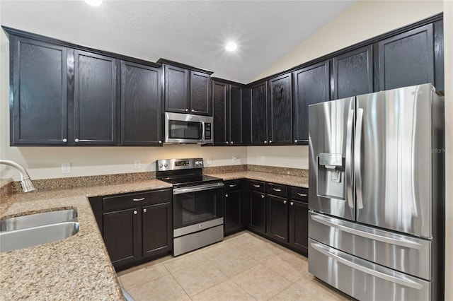 kitchen with light tile patterned floors, lofted ceiling, light stone countertops, stainless steel appliances, and a sink