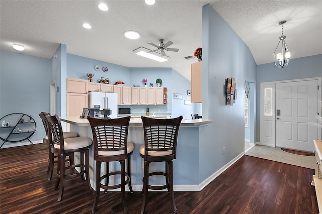 kitchen featuring light brown cabinets, lofted ceiling, a breakfast bar, dark hardwood / wood-style floors, and white refrigerator with ice dispenser