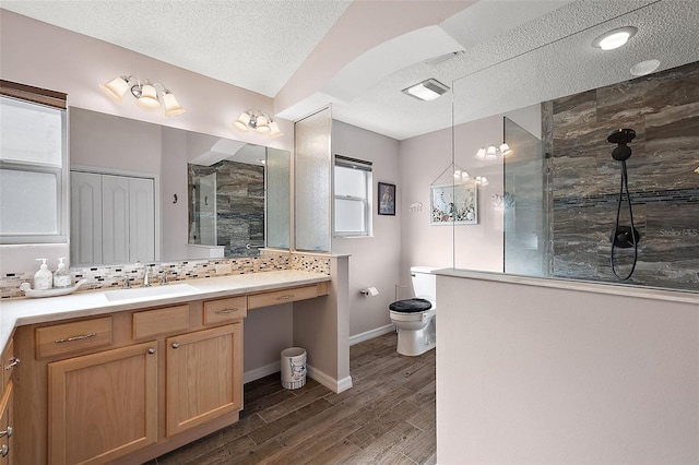 bathroom with a tile shower, a textured ceiling, hardwood / wood-style floors, toilet, and vanity