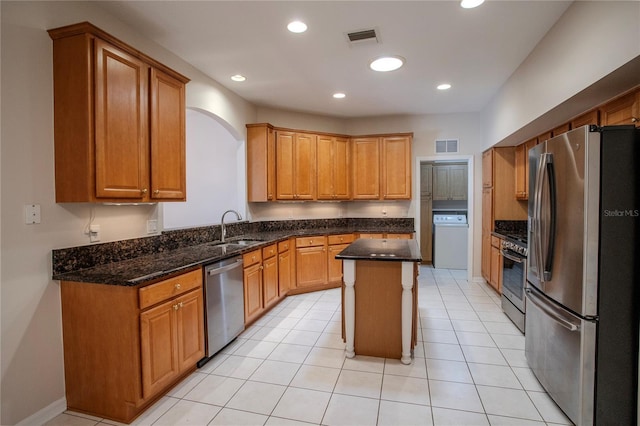 kitchen featuring a kitchen island, dark stone counters, light tile patterned flooring, sink, and stainless steel appliances