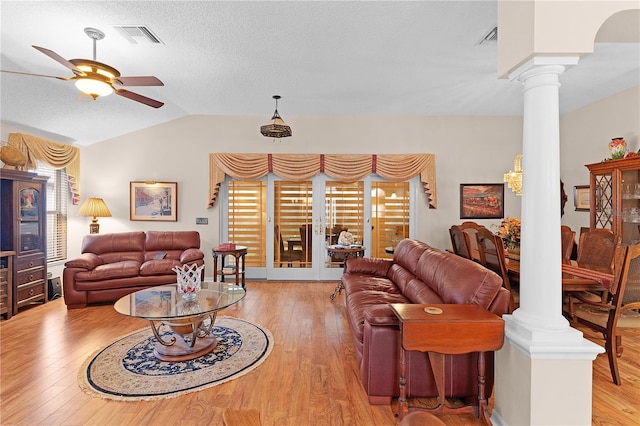 living room featuring decorative columns, ceiling fan, light wood-type flooring, and vaulted ceiling