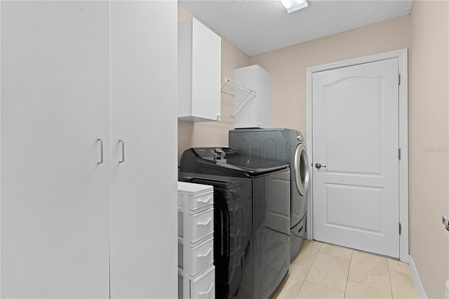 laundry area with cabinets, a textured ceiling, light tile patterned flooring, and washing machine and dryer